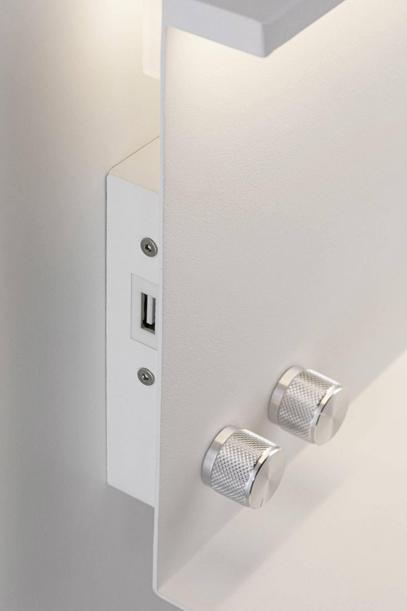 Eine weiße Wandhalterung mit USB-Anschluss und zwei silbernen Drehknöpfen, darüber eine LED-Leuchte.