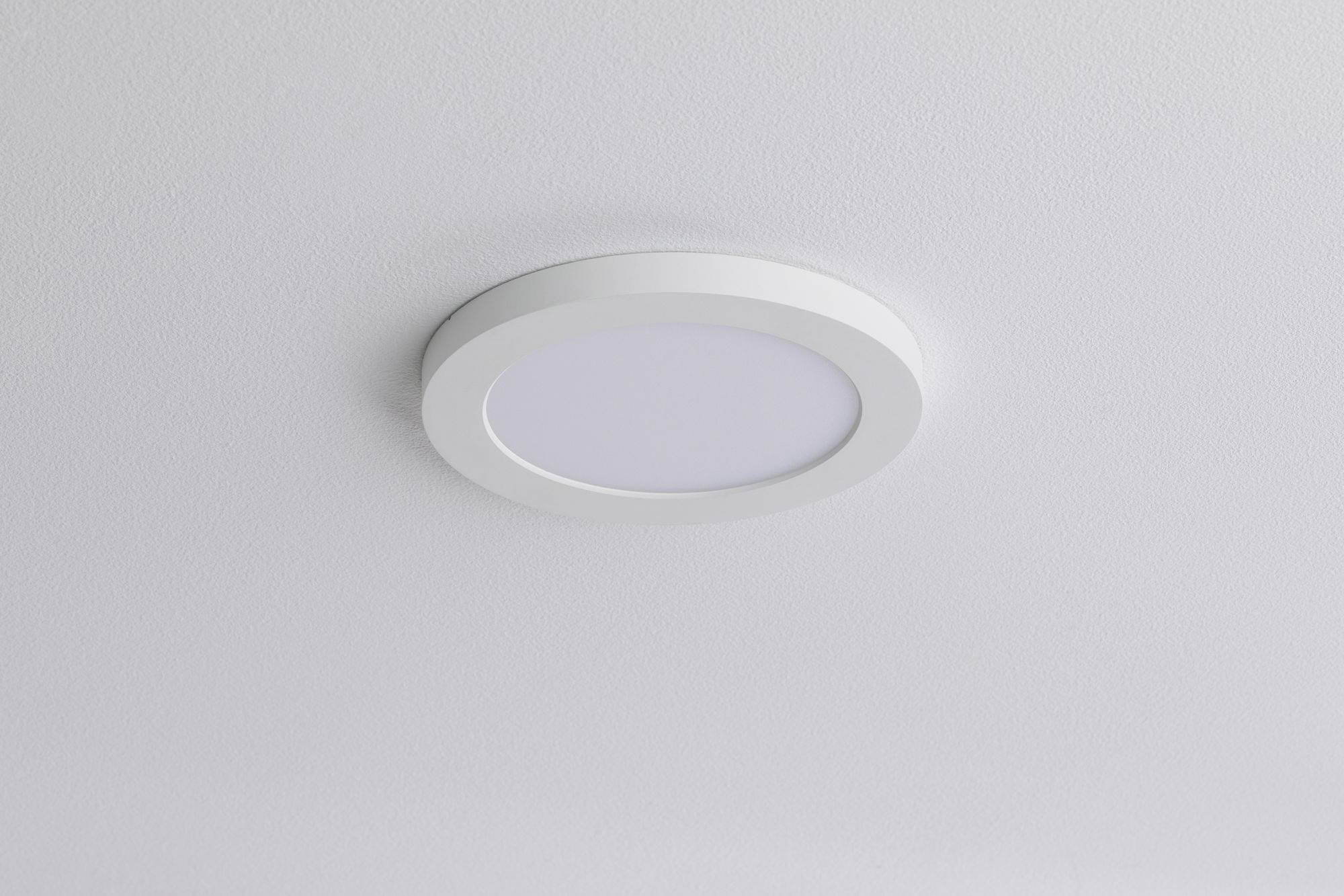 Runde Deckenleuchte aus Weißmetall mit schlichtem Design, montiert an einer weißen Decke. Sie dient zur allgemeinen Raumbeleuchtung.