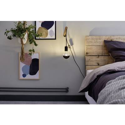 Gemütliches Schlafzimmer mit Holzbett, beleuchtet durch eine Lampe an der Wand. Zwei abstrakte Kunstwerke und eine Pflanze schmücken den Raum.
