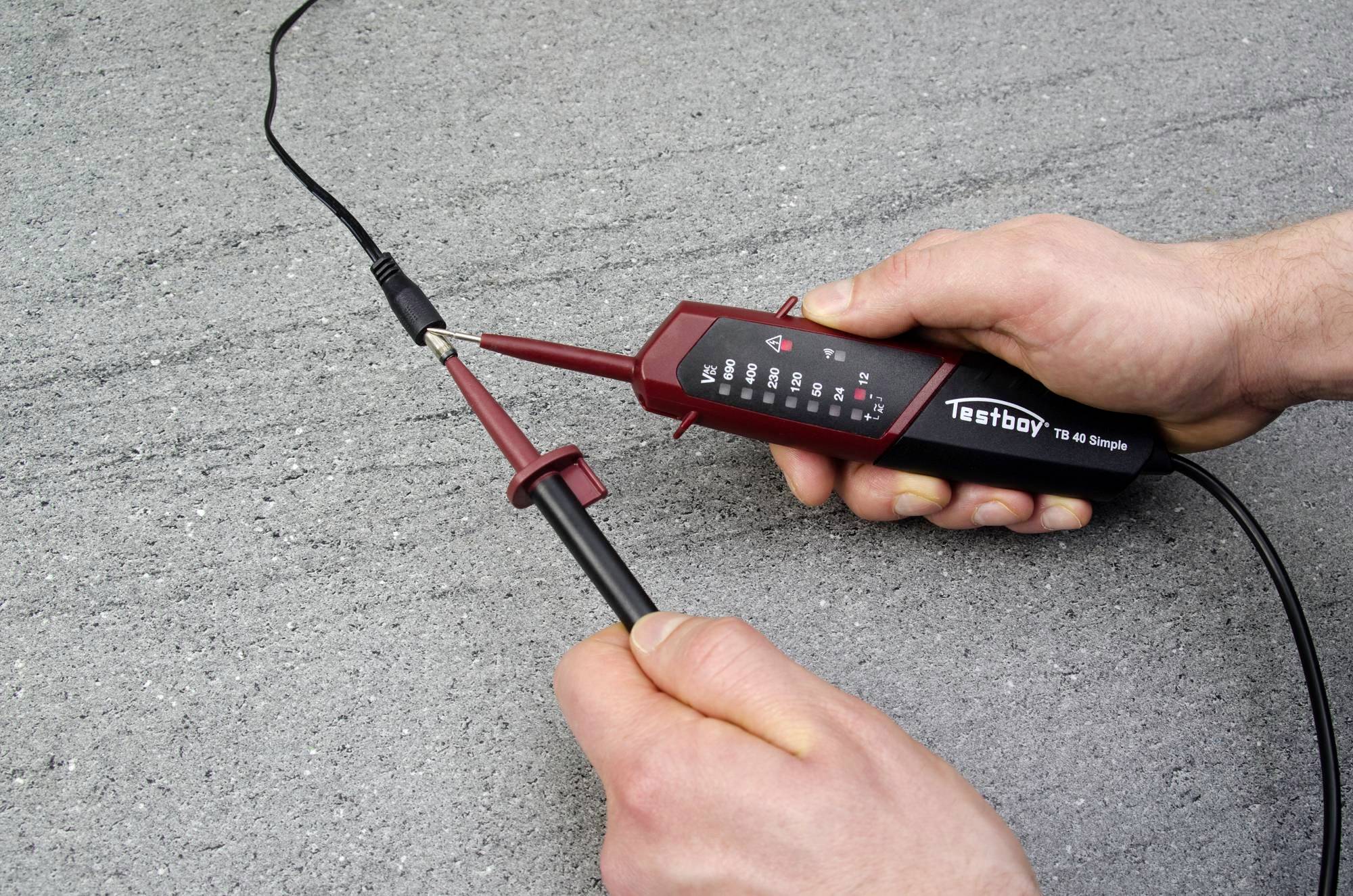 'Eine Person testet ein Kabel mit einem elektronischen Prüfgerät auf einer grauen Oberfläche. Fokus liegt auf den Prüfspitzen und dem Gerät.'