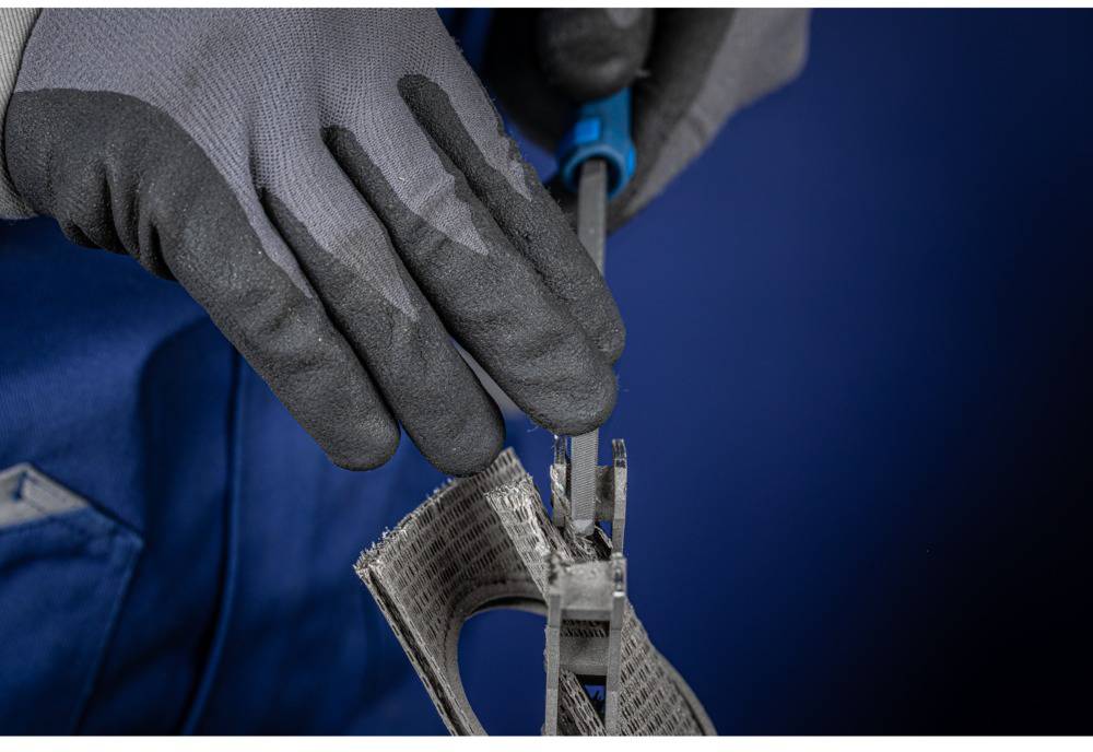 Person mit grauen Handschuhen hält eine Zange und bearbeitet ein Stück verstärktes Gewebe, möglicherweise zur Reparatur oder zum Bau.