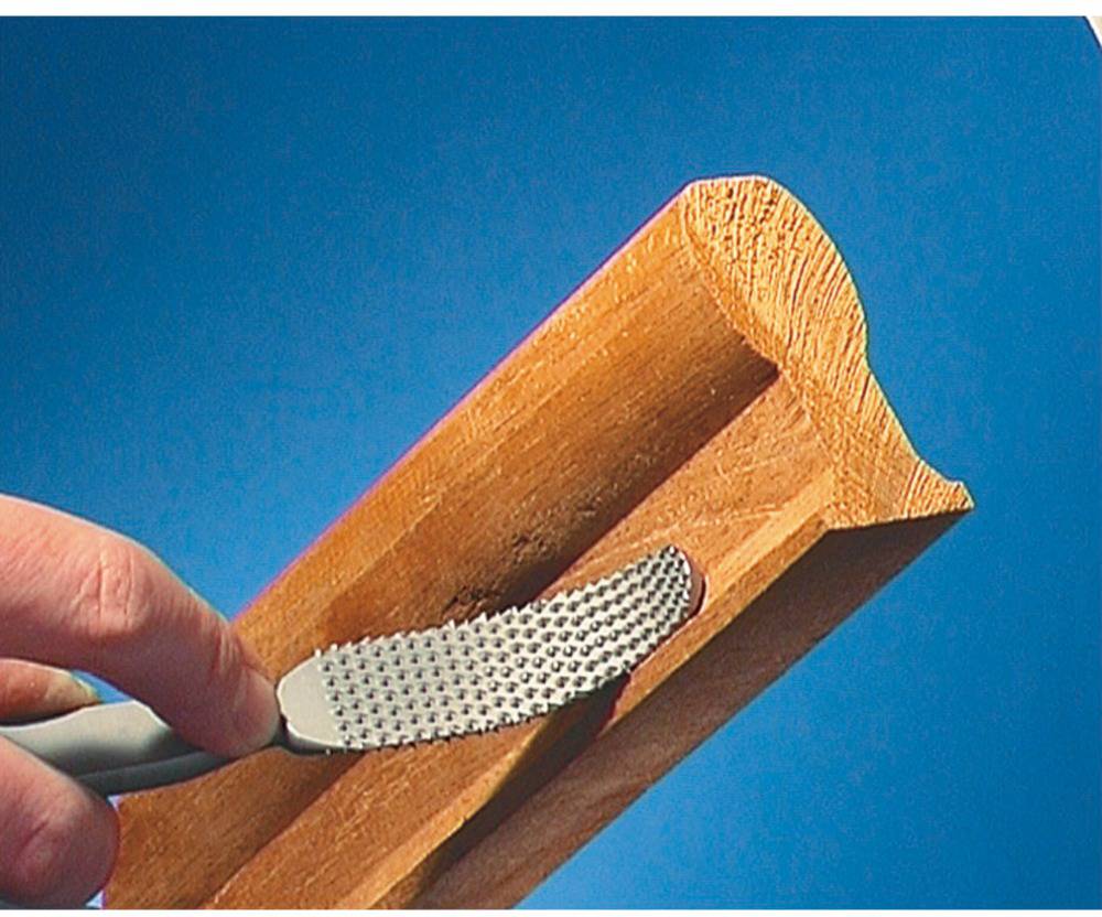 Hand hält eine Raspel und glättet ein Stück Holz mit einer dekorativen Kante. Hintergrund ist blau.