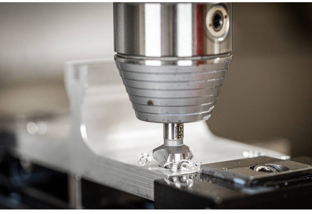 Großaufnahme einer CNC-Fräsmaschine, die ein Metallteil bearbeitet. Die Maschine ist in Aktion und erzeugt metallische Späne.