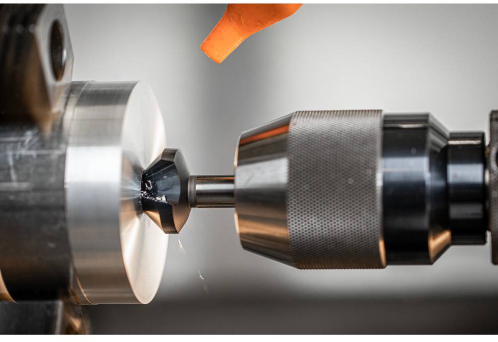 Eine Metallmaschine dreht ein Werkstück, Funken fliegen. Eine orange Flüssigkeitszufuhr weist auf Kühlung hin.