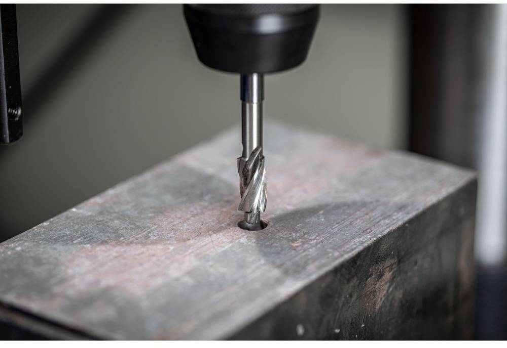 Bohrer bohrt ein Loch in einen Metallblock. Der Spiralschaft des Bohrers ist sichtbar. Industrielle Nutzung wird angedeutet.