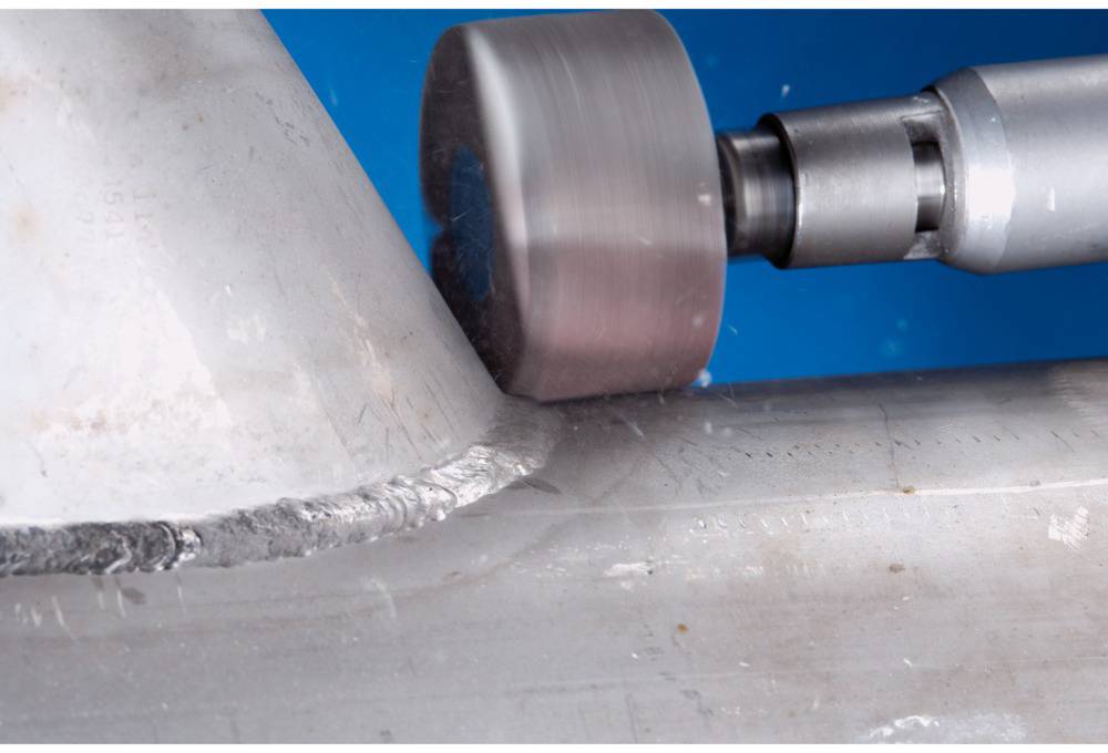 Eine Metalloberfläche wird mit einem rotierenden Werkzeug abgeschliffen. Der Hintergrund ist blau.