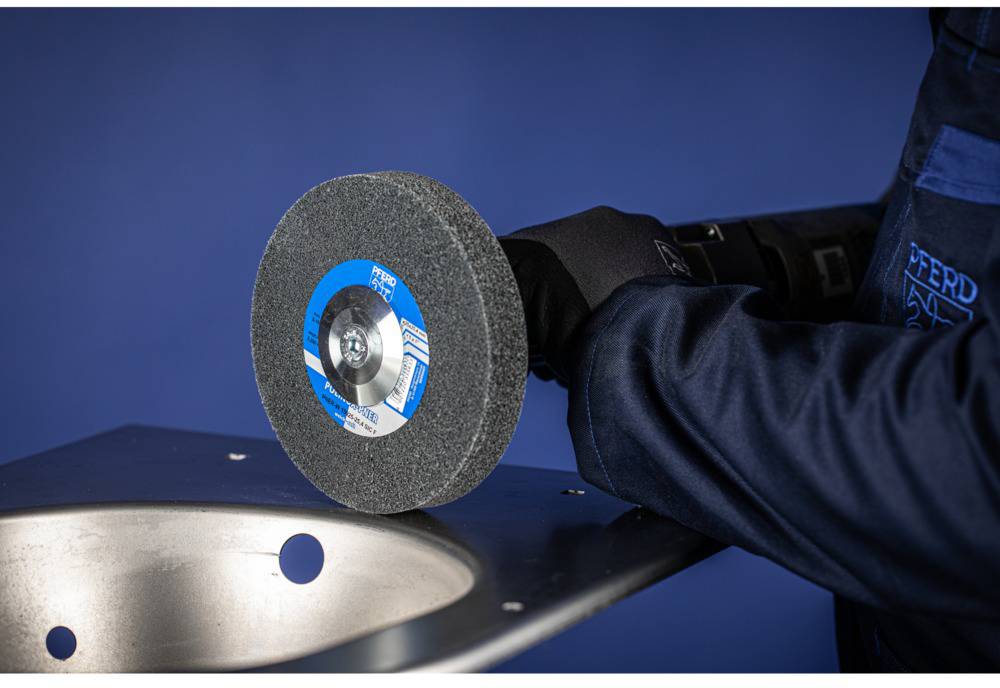 Eine Person schleift mit einer Schleifscheibe ein Metallblech. Die Szene zeigt einen Nahblick auf das Werkzeug und den Arbeitsvorgang.