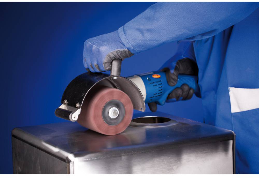 Eine Person in blauer Arbeitskleidung schleift mit einem Winkelschleifer eine Metalloberfläche. Handschuhe werden zum Schutz getragen.