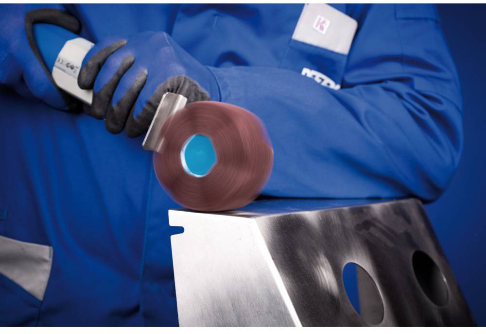 Person in blauem Schutzanzug schleift eine Metallfläche mit einem rotierenden Werkzeug.