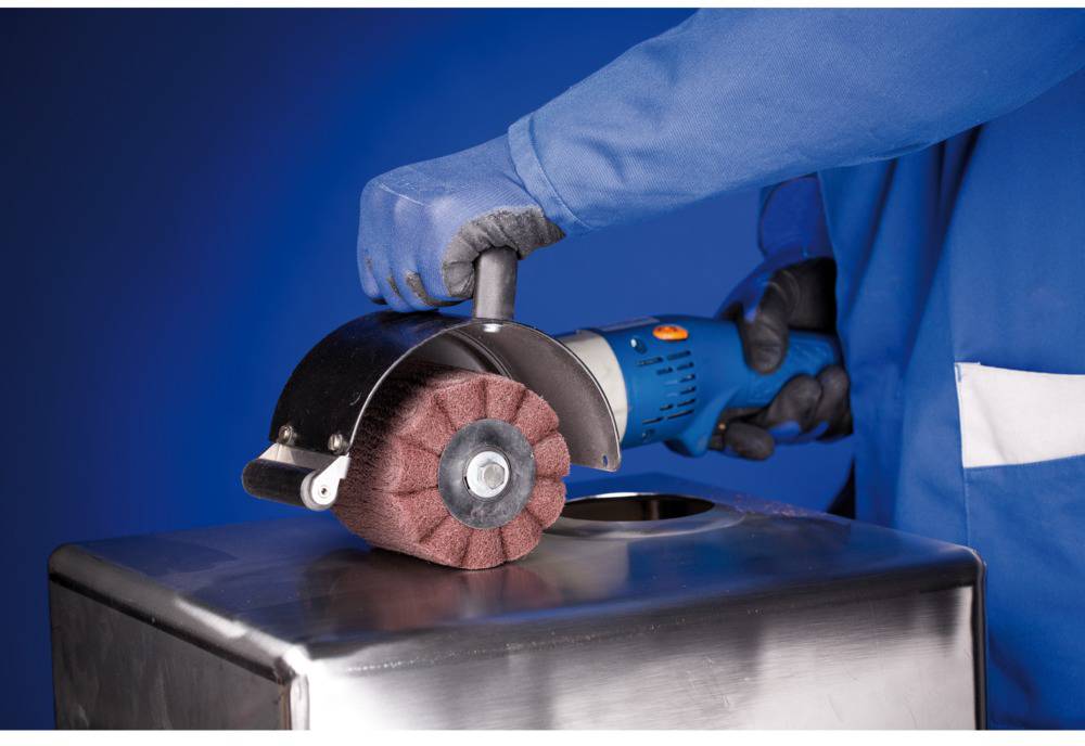 Eine Person schleift eine Metalloberfläche mit einem Elektrowerkzeug, das eine runde, bürstenartige Schleifscheibe hat.