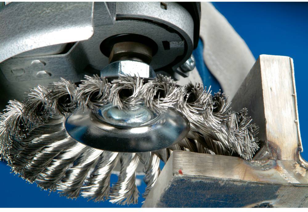Eine Drahtbürste poliert die Oberfläche eines Metallstücks. Die Szene zeigt industrielles Polieren auf einem blauen Hintergrund.