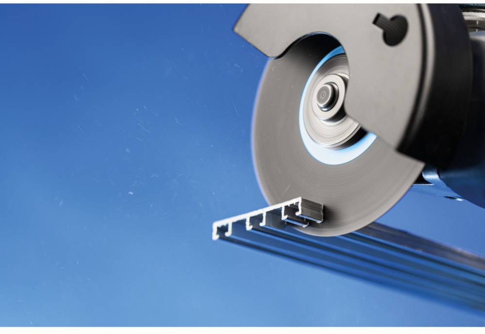 Ein Winkelschleifer schneidet ein Aluminiumprofil. Die Maschine arbeitet präzise, während Metallsplitter in der Luft schweben.