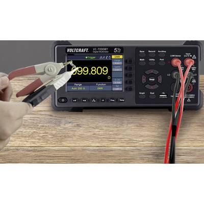 Digitalmultimeter auf Holztisch zeigt '999.809' an. Clip-Messleitungen an Anschlüssen. Links eine Hand beim Messen.