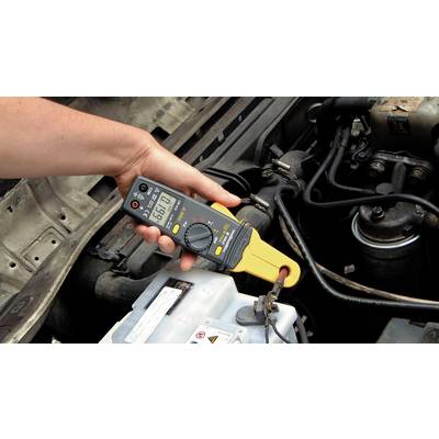 Eine Hand hält ein Multimeter, das auf 12,6 Volt eingestellt ist, und misst die Spannung einer Autobatterie im Motorraum.