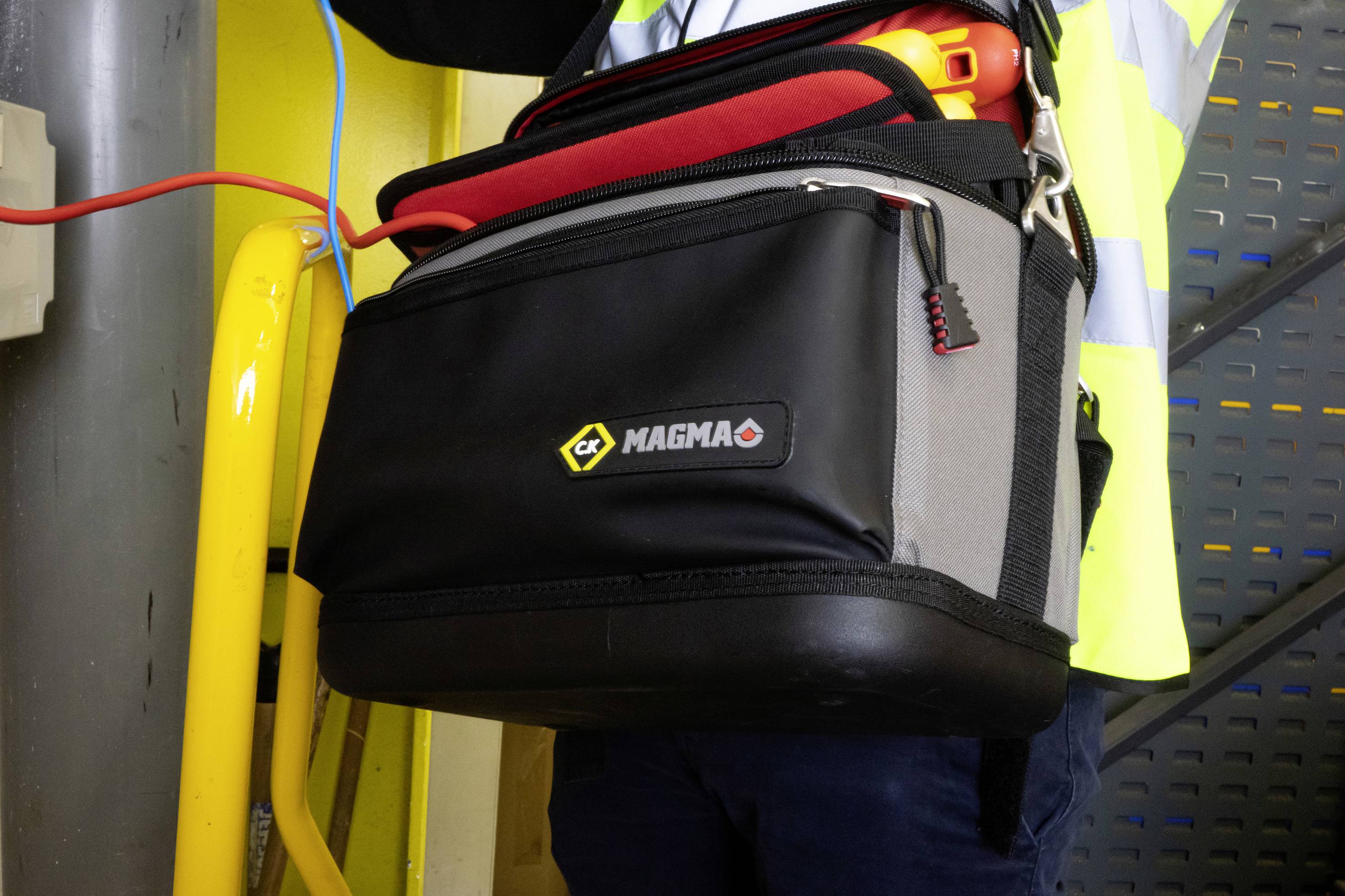 'Werkzeugtasche mit CX Magma-Logo, getragen von Person in Sicherheitsweste, umgeben von gelben Sicherheitsbalken und Kabeln.'