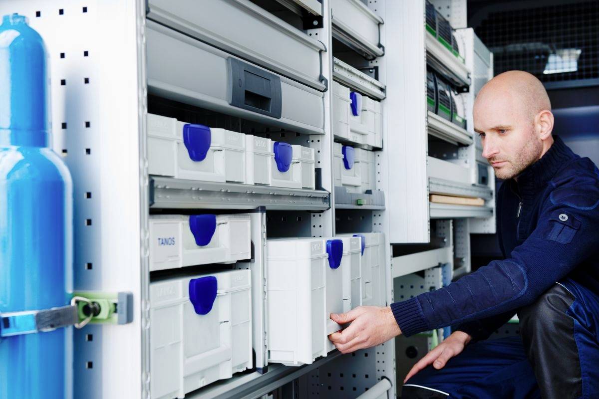 Ein Mann ordnet Lagerkisten in einem Fahrzeug an, das mit Regalen und verschiedenen Werkzeugen ausgestattet ist.