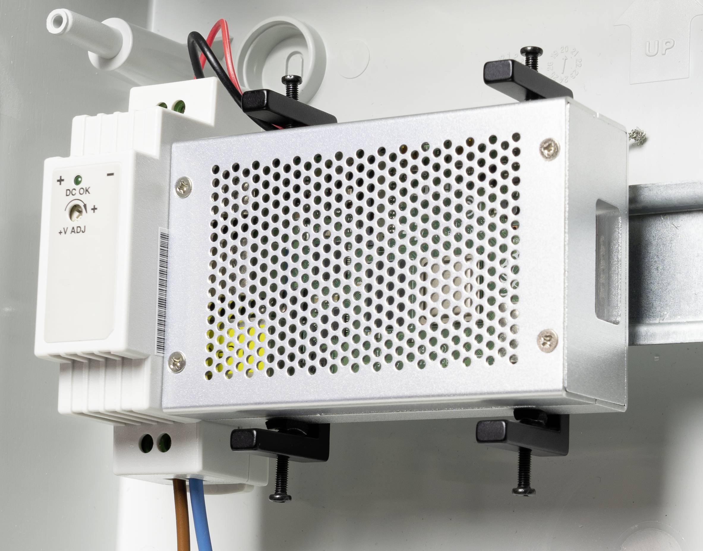 'Metallene, perforierte Abdeckung einer elektrischen Komponente, befestigt mit Schrauben. Daneben ein kleines weißes Modul mit einer grünen LED.'