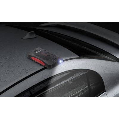 Ein tragbares Starthilfegerät mit eingeschalteter Taschenlampe liegt auf einem verregneten Autodach.