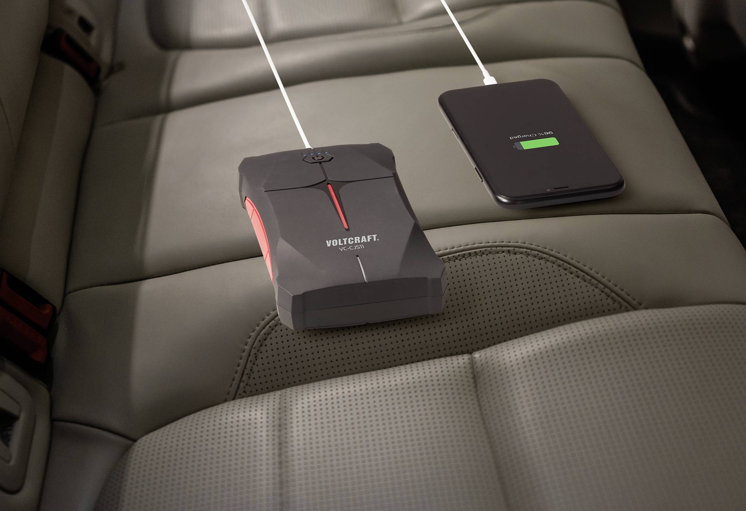 Eine Powerbank lädt ein Smartphone auf einem Autositz auf.