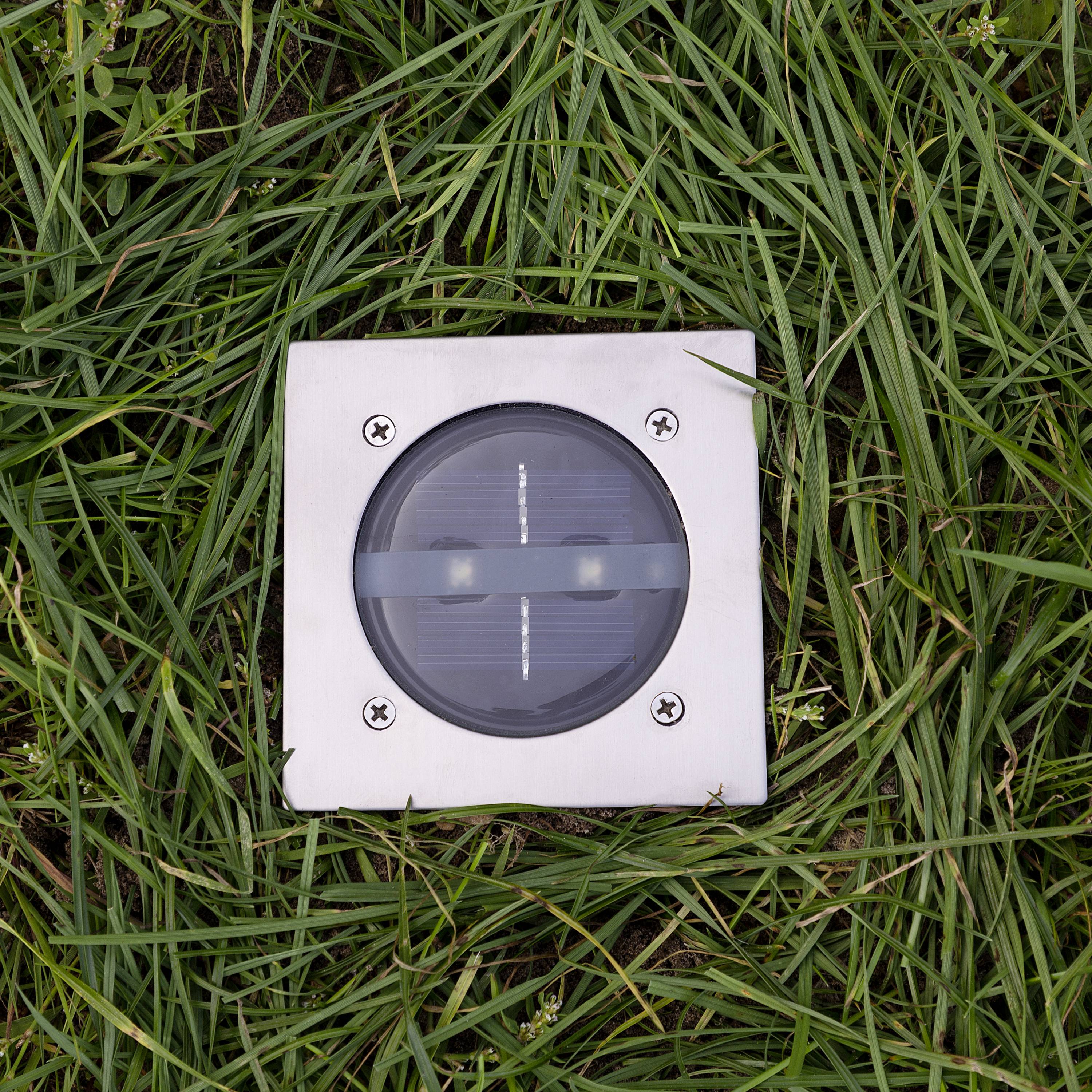 Ein quadratisches Solarmodul mit einem Metallrahmen ist in einer Grasfläche eingebaut.