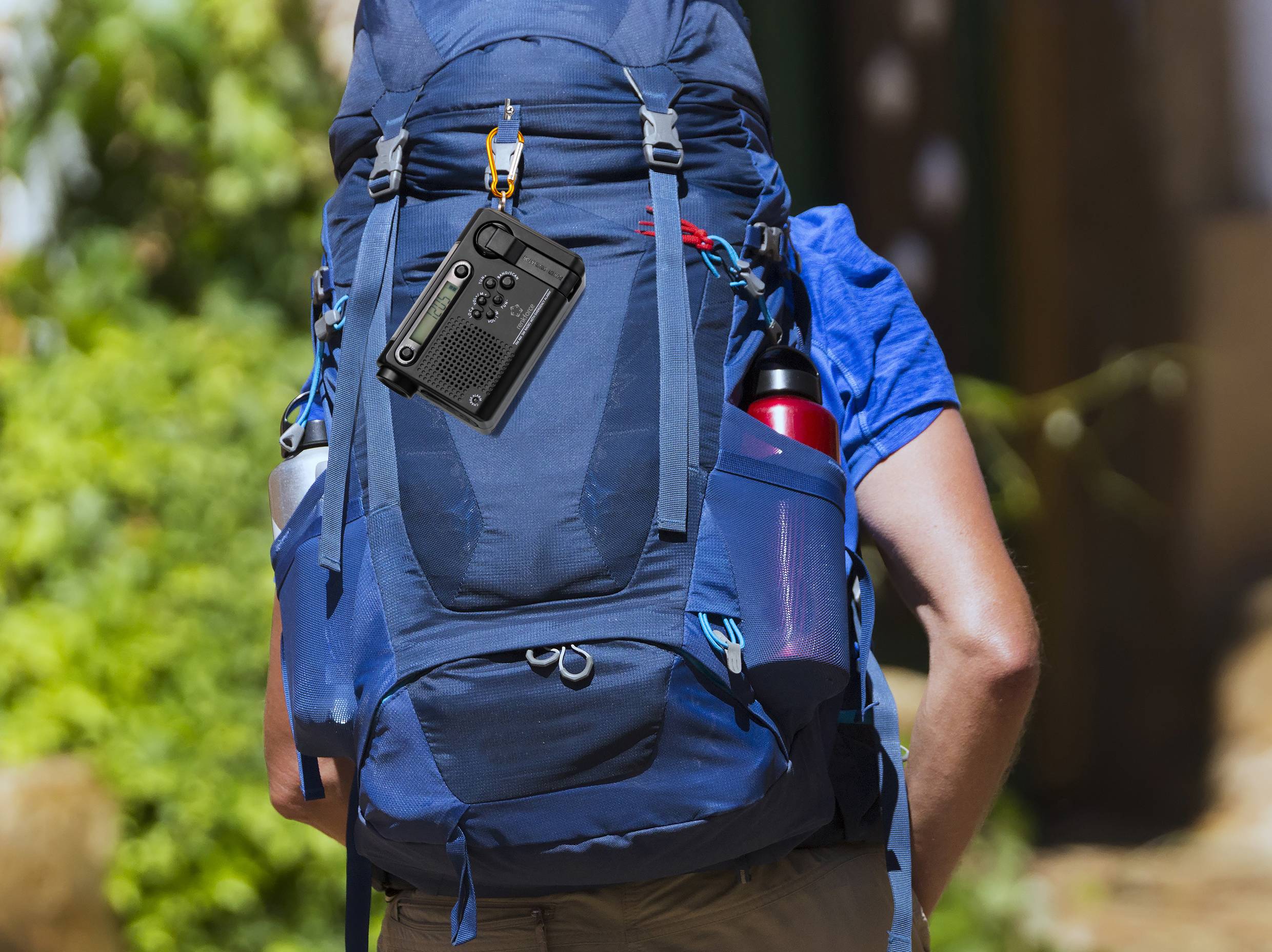 Eine Person trägt einen großen, blauen Rucksack mit einer schwarzen Kamera an der Seite. Im Hintergrund sind Bäume und Gebäude zu sehen.