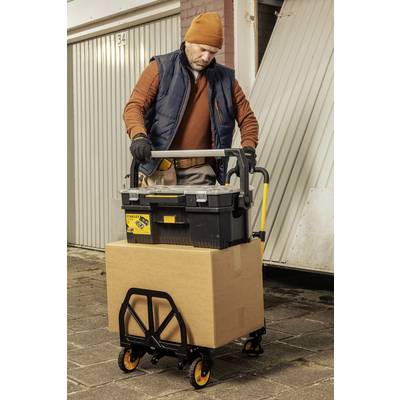 Ein Mann transportiert mit einem Handwagen eine Werkzeugkiste und einen großen Karton vor einer Garagenwand.