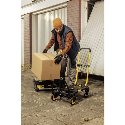 Ein Mann hebt einen großen Karton vor einer Garagentür. Neben ihm steht ein gelber Handwagen auf einem gepflasterten Weg.