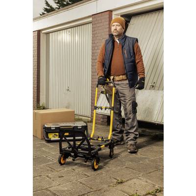 Ein Mann in Arbeitskleidung steht mit einem Handwagen vor einer offenen Garagentür. Neben ihm liegen eine Kiste und ein Karton.