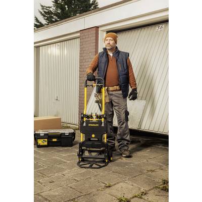 Ein Handwerker steht vor einer Garage und hält einen Handwagen mit Werkzeugkiste. Er trägt eine Mütze und Arbeitskleidung.