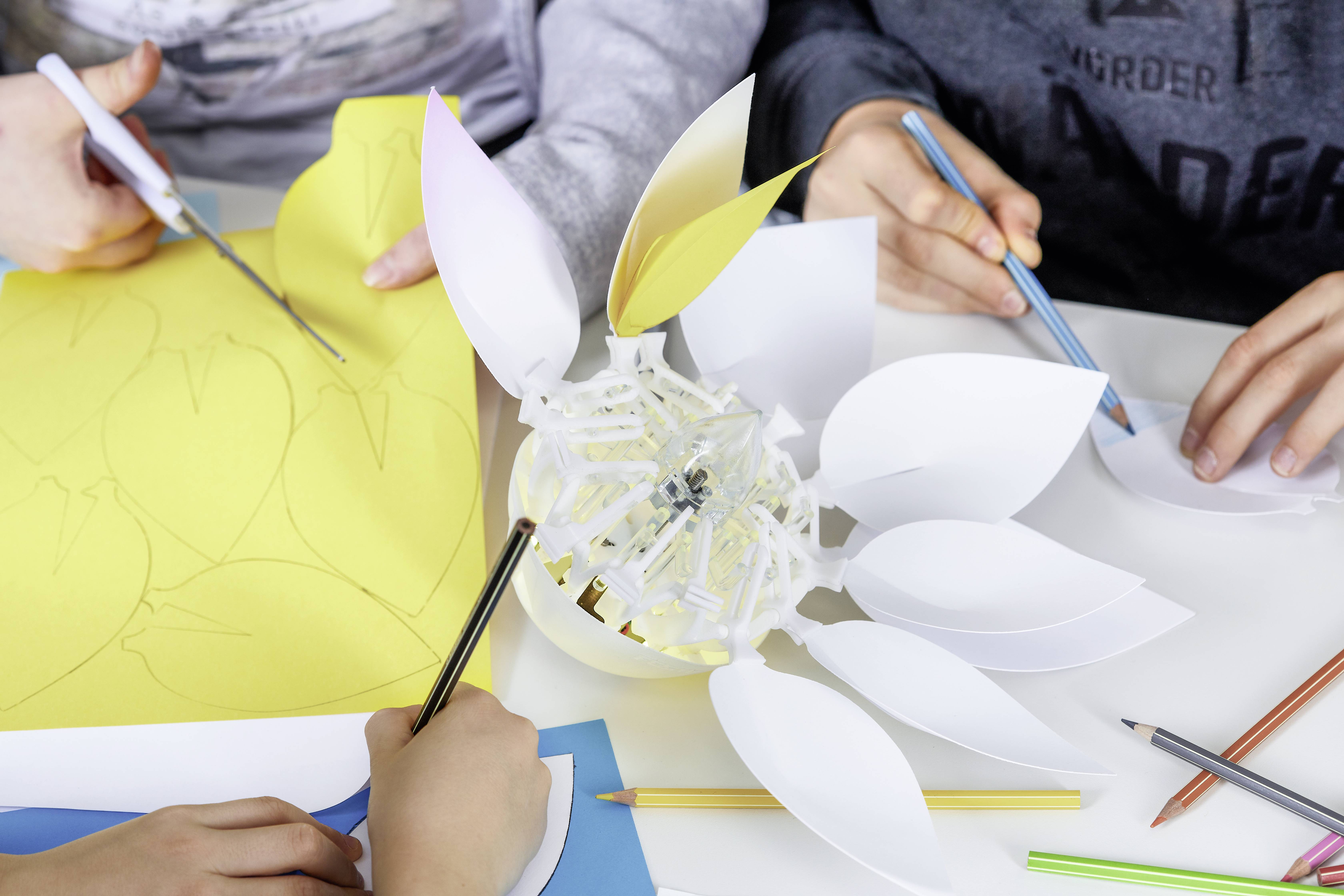 Kinder basteln eine Blume aus Papier. Verschiedene Schablonen und Buntstifte liegen auf dem Tisch. Kreatives Gruppenprojekt.