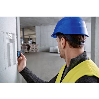 Ein Bauarbeiter mit blauem Helm und gelber Weste verwendet ein Laser-Entfernungsmessgerät an einer Betonwand in einer Baustelle.
