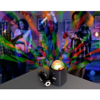 Eine bunte Partyszene mit vier Personen, die tanzen. Im Vordergrund steht eine leuchtende Lampe mit USB-Anschluss auf einem Tisch.