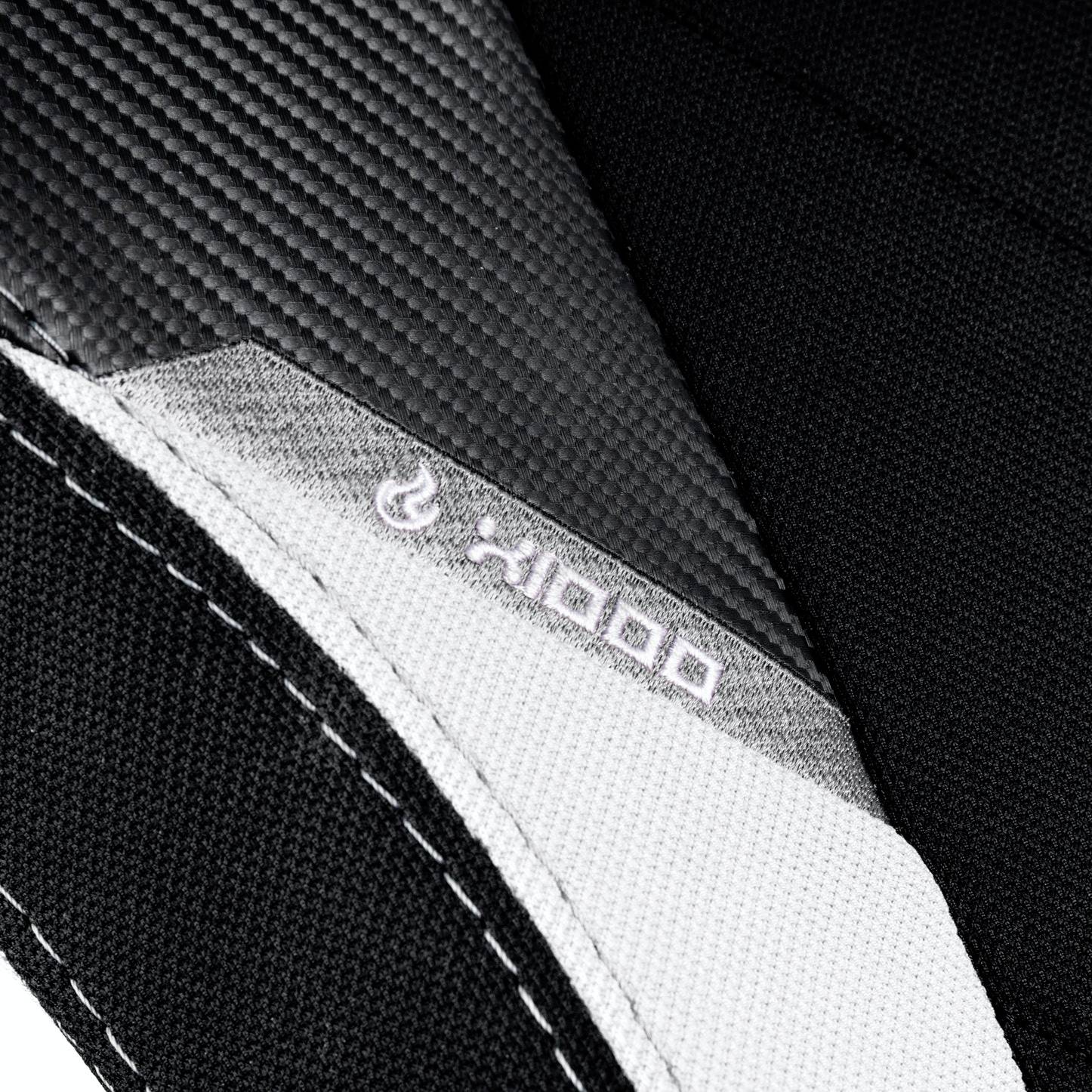 Teil von Stoff und Textilmaterial in Schwarz, Weiß und Grau, mit sichtbarer Naht und Logo eines Herstellers auf der weißen Fläche.