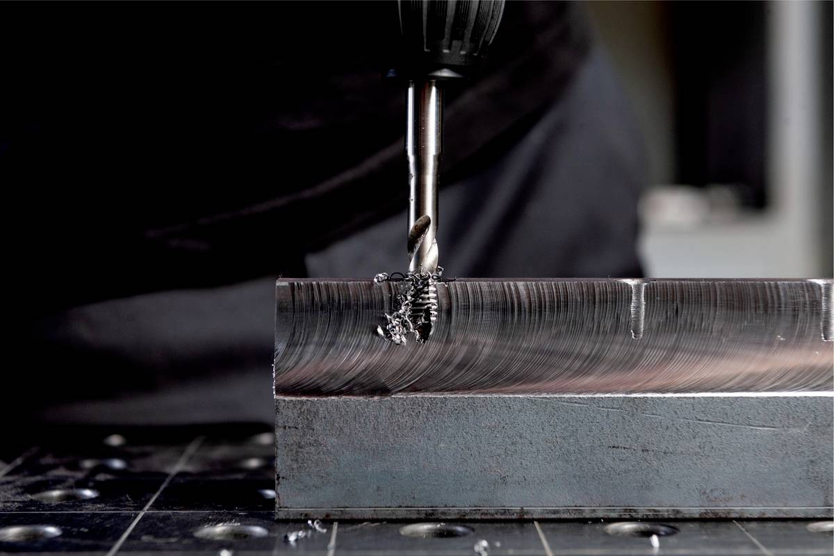 Ein Bohrer bearbeitet ein Metallblock, wobei Späne entstehen. Der Fokus liegt auf dem präzisen Bohren und der Oberfläche des Metalls.