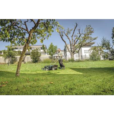 Ein Mann mäht an einem sonnigen Tag den Rasen in einem Garten, umgeben von Bäumen und modernen Wohnhäusern im Hintergrund.