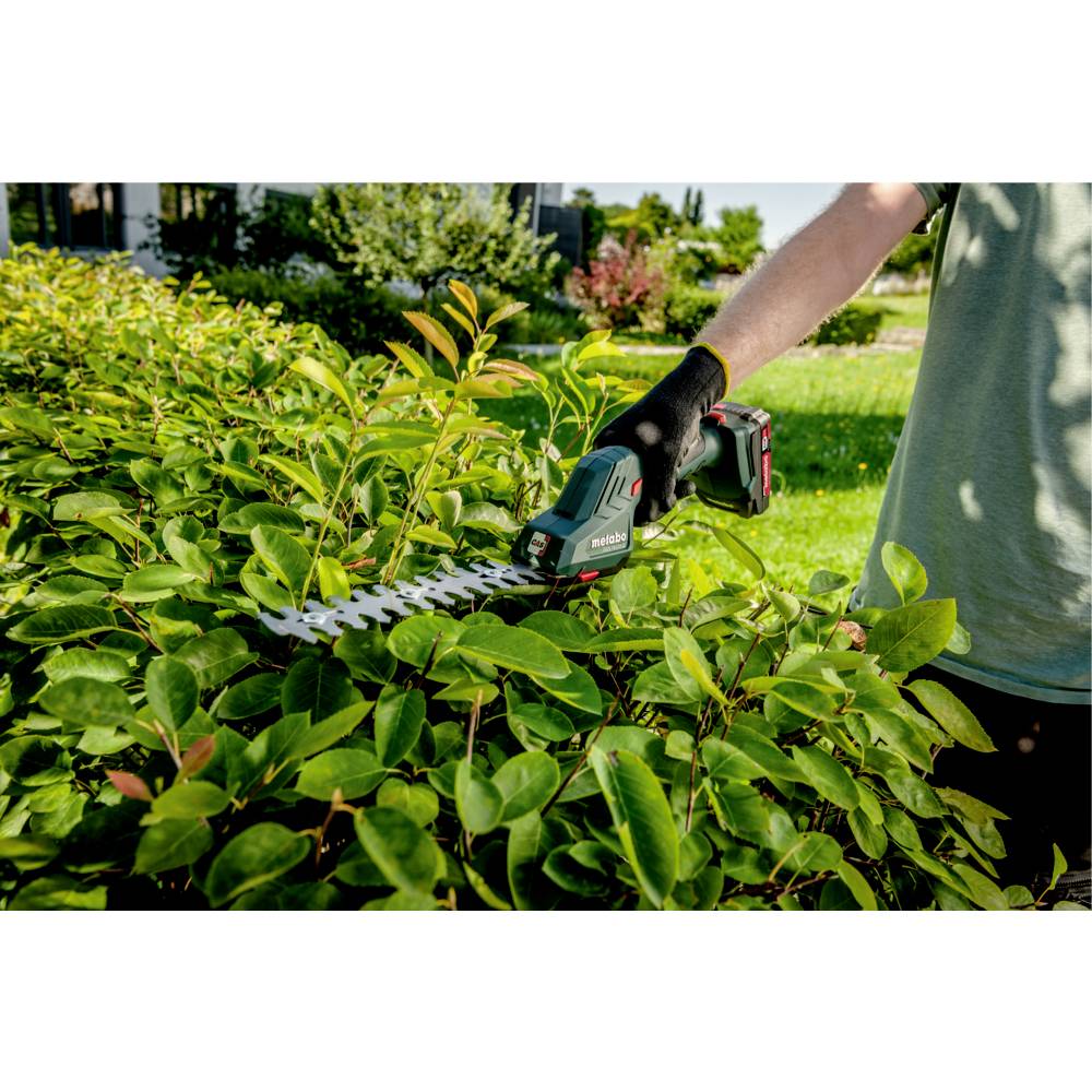 Person, die eine grüne Hecke mit einem tragbaren elektrischen Heckenschneider in einer Gartenumgebung trimmt.