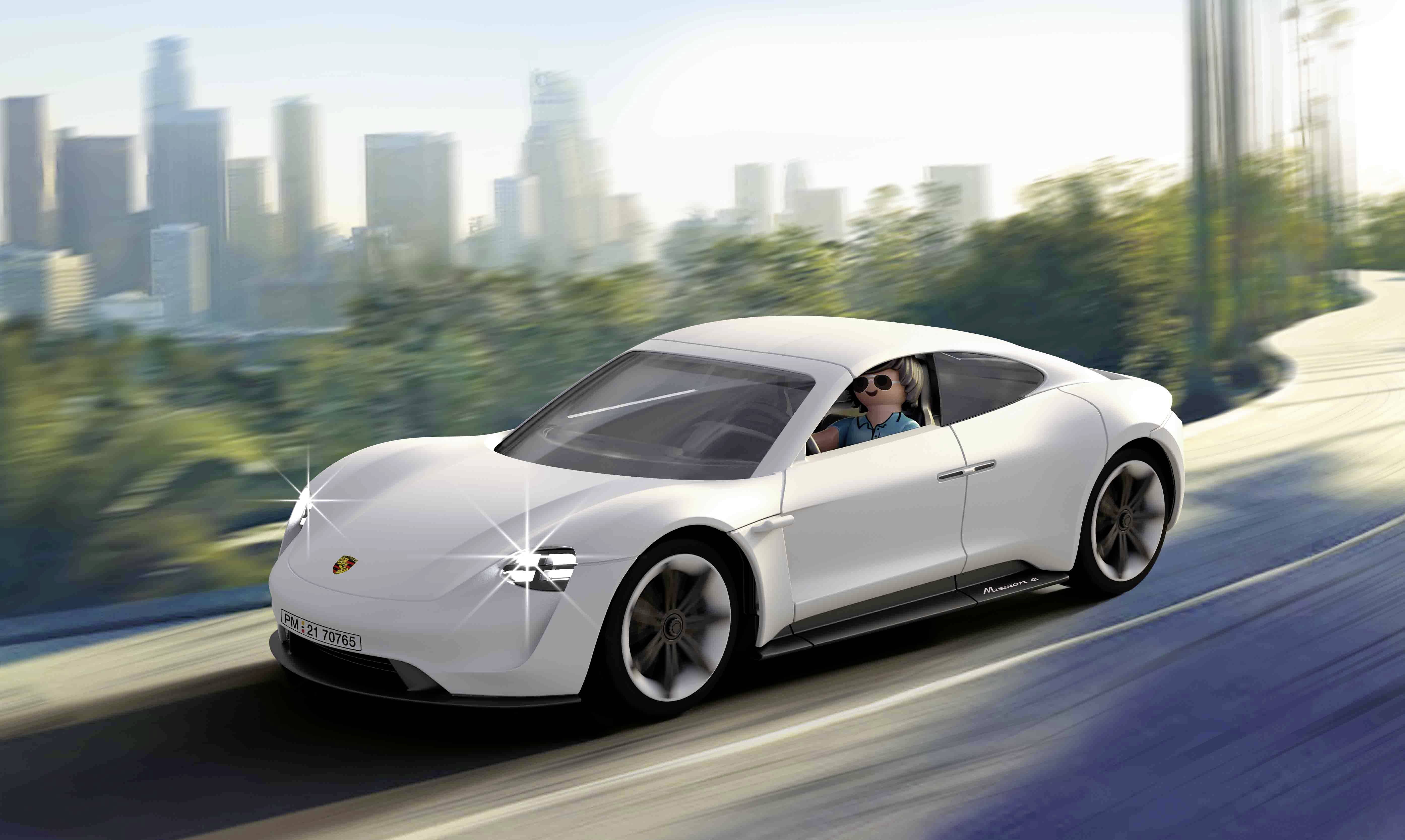 Ein weißes Sportauto fährt auf einer Straße in einer städtischen Umgebung. Im Hintergrund sind verschwommene Wolkenkratzer zu sehen.