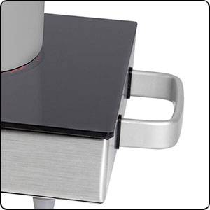 Ein Wasserkocher steht auf einer schwarzen, quadratischen Induktionskochplatte. Ein silberner Griff ist an der Seite sichtbar.