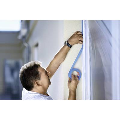 Ein Mann klebt blaues Klebeband an eine Hauswand. Er trägt ein weißes T-Shirt und eine Armbanduhr. Die Umgebung ist unscharf.