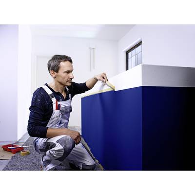 Eine Person in einem Arbeitsanzug streicht eine Innenwand. Die untere Hälfte der Wand ist blau, die obere Hälfte weiß.