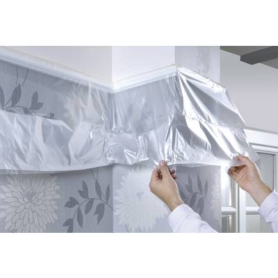 Zwei Hände befestigen silberne Stoßschutzecke an blumig gemusterter Wand.
