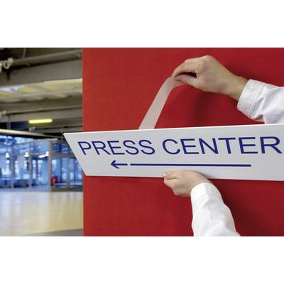Person befestigt Schild mit Aufschrift 'PRESS CENTER' an roter Wand in einem Gebäude. Zeigt Richtung mit Pfeil links.