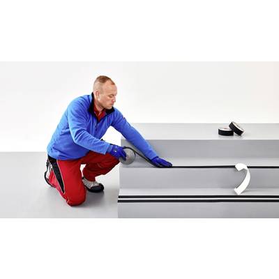 Ein Mann kniet und bringt rutschfeste Streifen auf eine Treppenstufe auf. Er trägt Arbeitskleidung und Schutzhandschuhe.