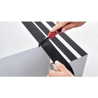 Eine Person schneidet mit einem Cutter-Messer schwarze Anti-Rutsch-Streifen auf eine weiße Oberfläche.