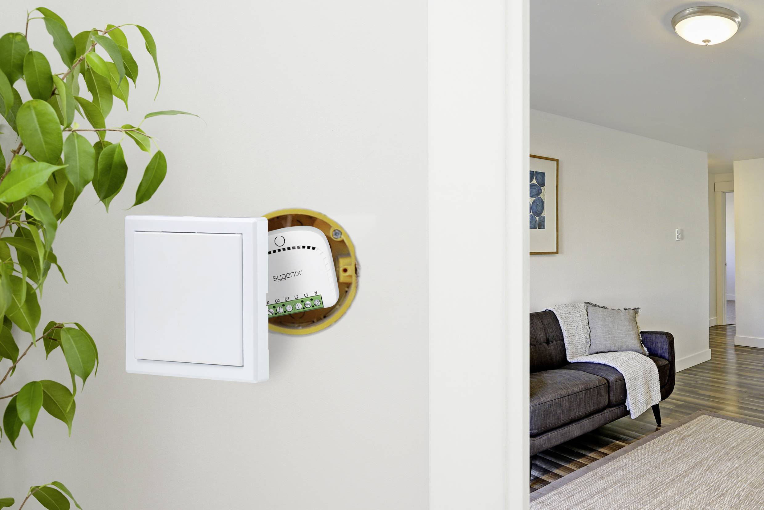 Ein Wohnzimmer mit einer offenen Wand, die einen verdeckten Sicherungskasten zeigt. Ein graues Sofa mit einer Decke ist sichtbar.