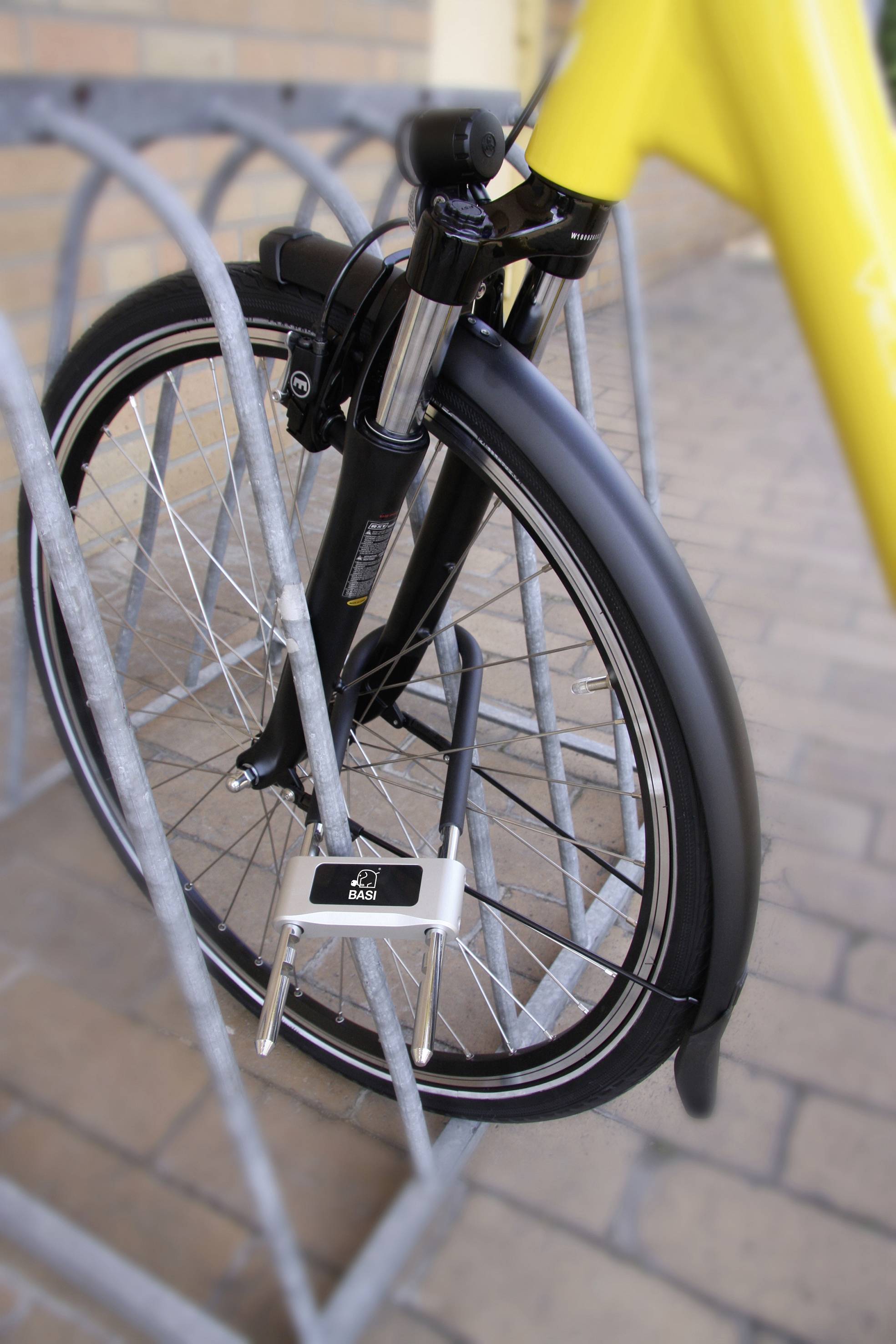 Ein gelbes Fahrrad ist an einem Ständer mit einem U-Schloss festgeschlossen. Der Fokus liegt auf dem Vorderrad und dem Schloss.