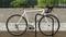 Ein weißes Fahrrad ist an einem Metallfahrradständer angeschlossen, im Hintergrund eine Mauer mit grüner, verschwommener Landschaft.