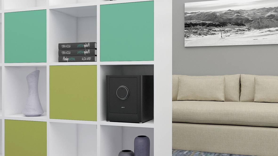 Regal mit bunten Fächern, einige Bücher, Vase und schwarzer Tresor; daneben beiges Sofa, an der Wand ein Bild in Grautönen.