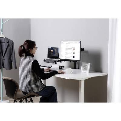 Frau arbeitet an einem Schreibtisch mit Laptop und Monitor. Die Umgebung ist modern und ordentlich, mit einem hängenden Blazer im Hintergrund.