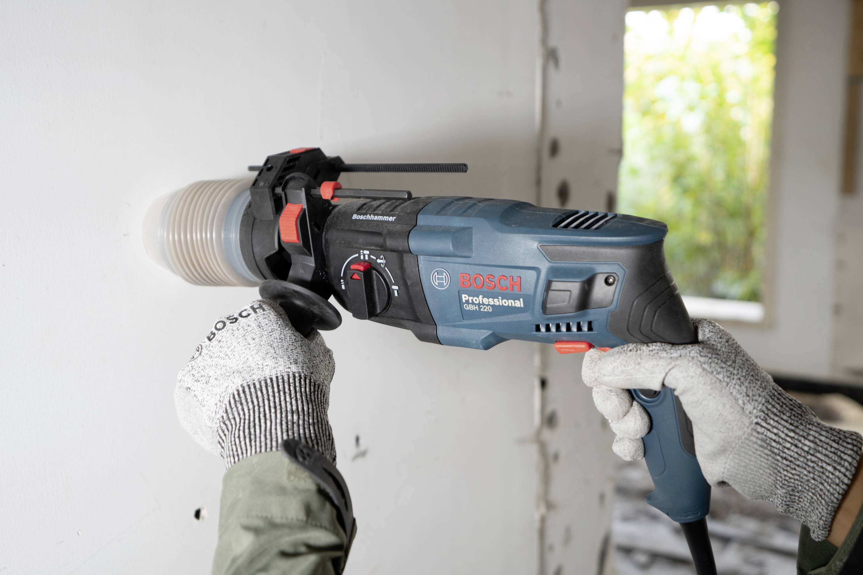 'Person verwendet einen Bosch-Profibohrer, um in einer weißen Wand ein rundes Loch zu bohren. Hintergrund zeigt Baustelle.'